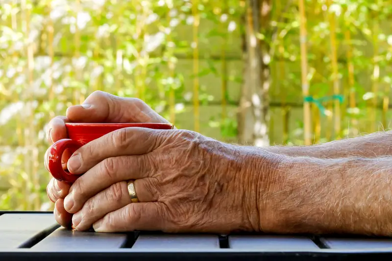 Mans d’una persona gran amb una tassa de cafè en una terrassa